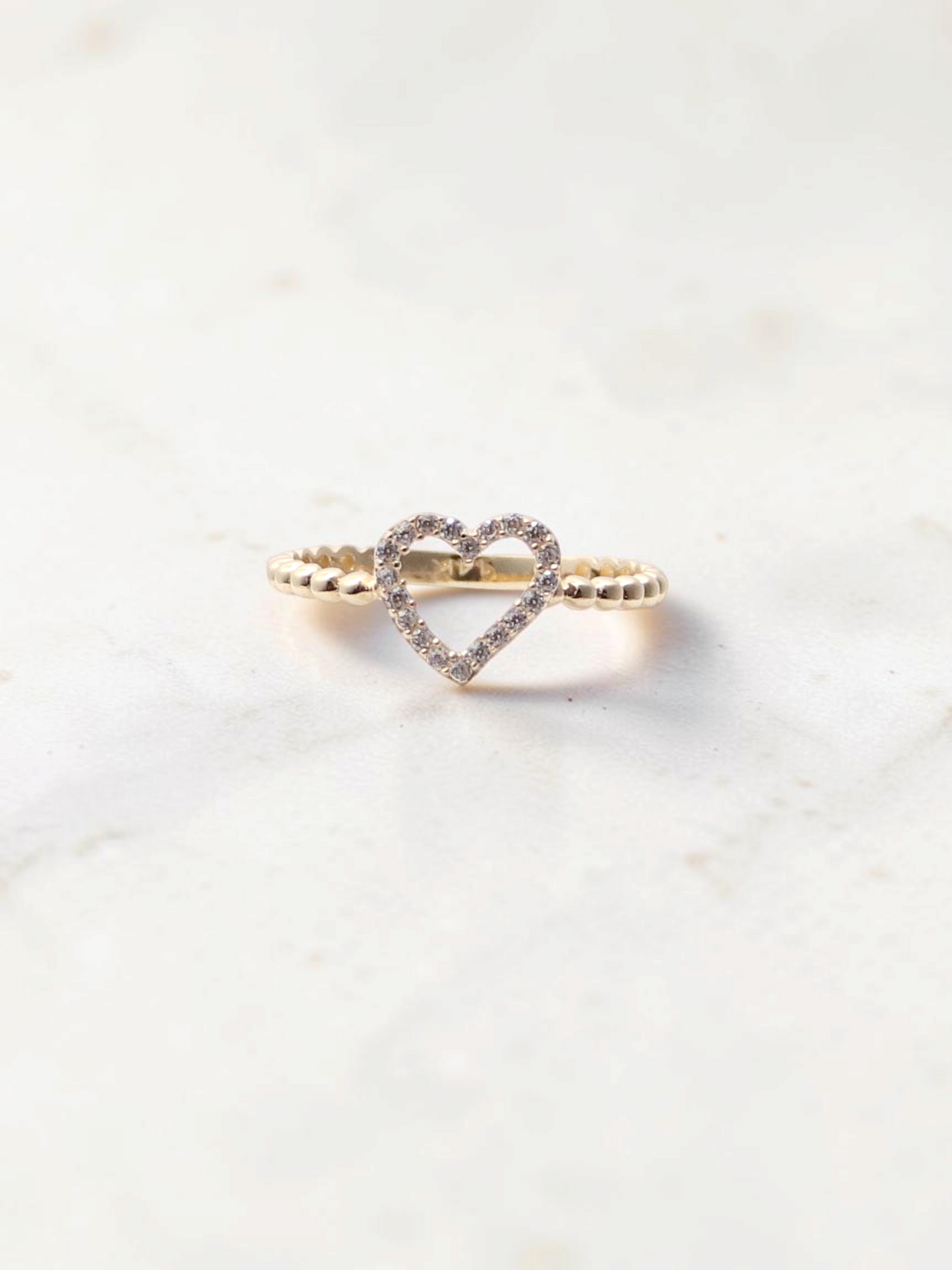 Zafrah 14k yellow gold heart ring featuring a beaded band and sparkling CZ stones on a marble surface.