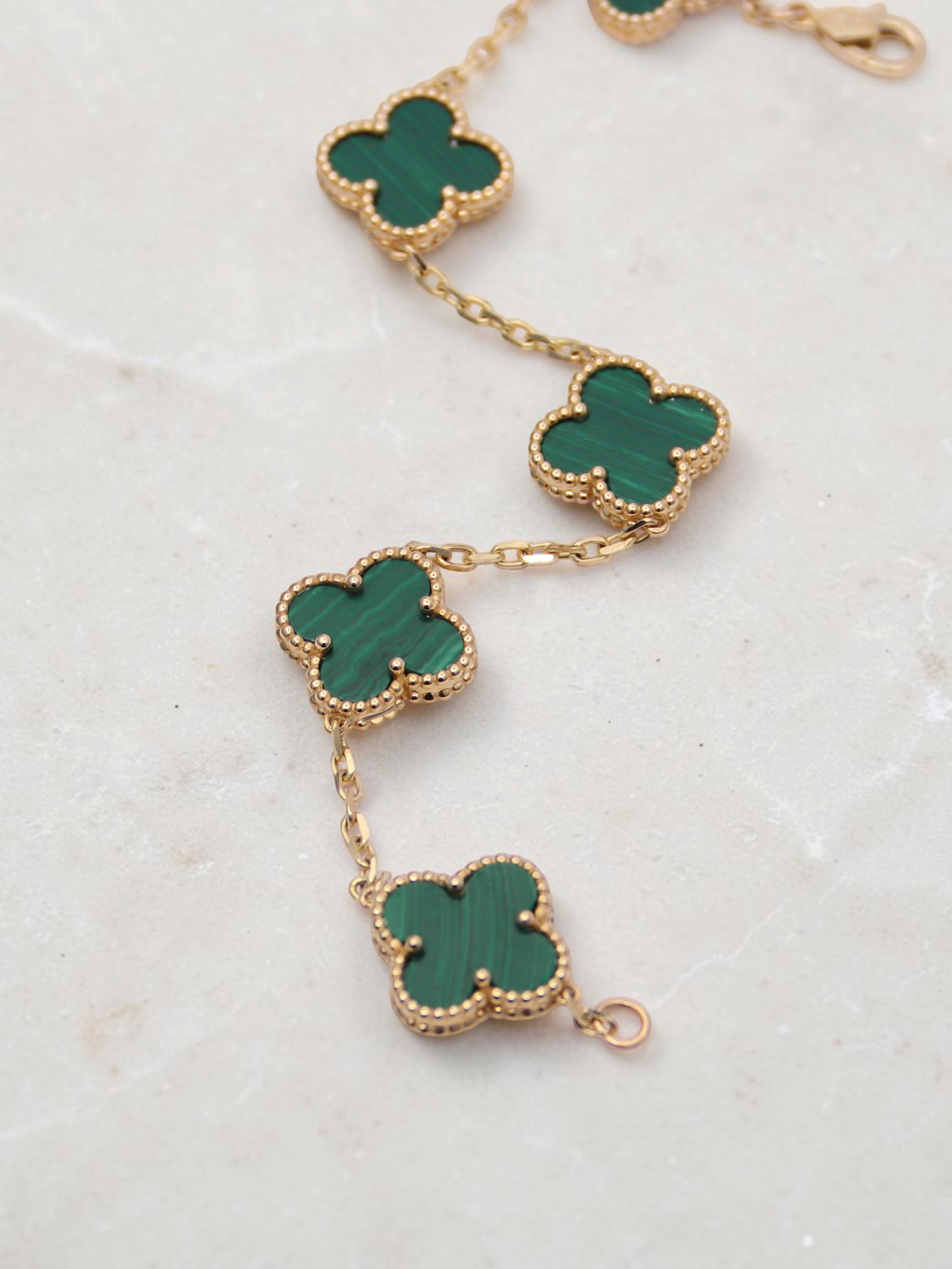 Zafrah 14k yellow gold bracelet featuring five green malachite clover motifs with beaded edges on a delicate chain.