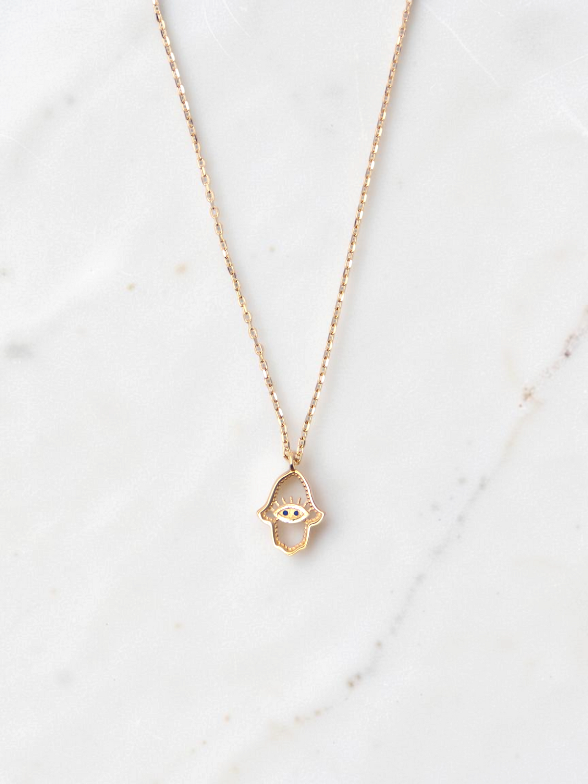 Zafrah 14k yellow gold hamsa eye pendant necklace with two small blue stones on a delicate round link chain