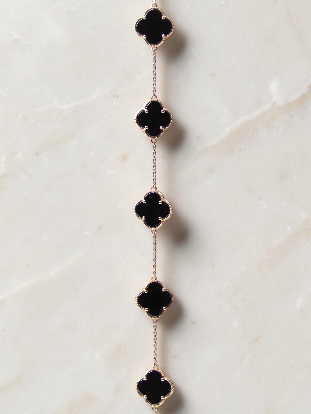 Zafrah bracelet featuring five black onyx clover motifs on a delicate gold chain against a white background.