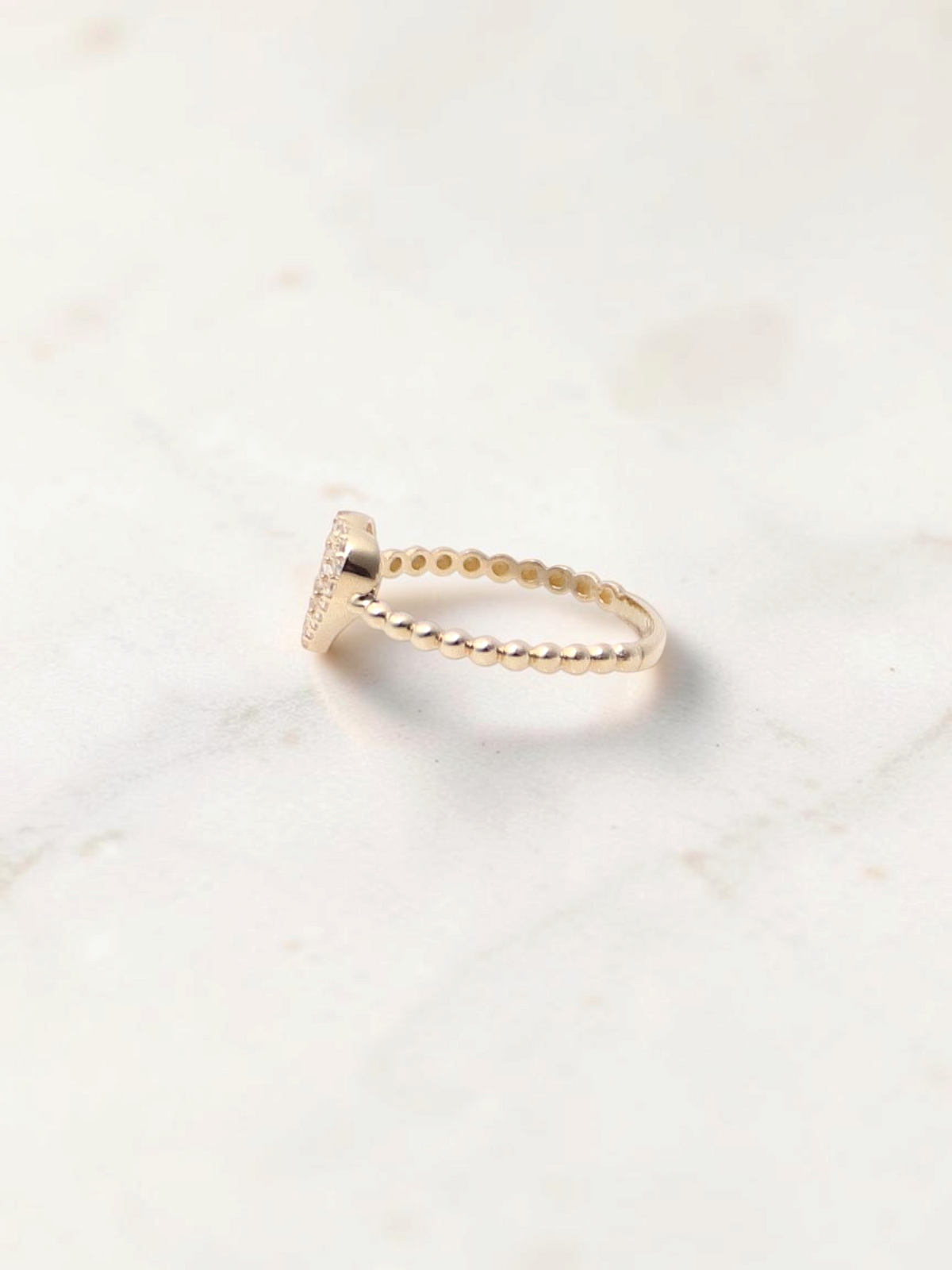 Zafrah 14k yellow gold heart bead ring with sparkling CZ stones on a white marble surface