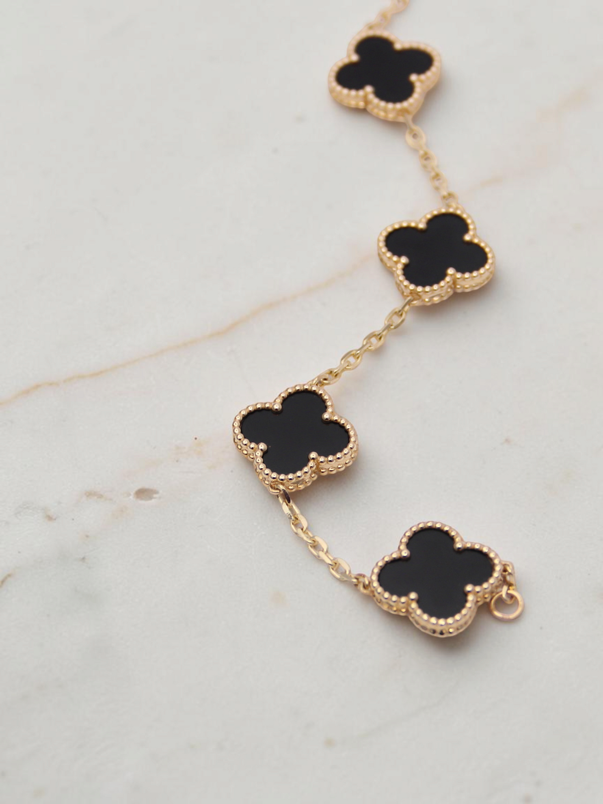 Zafrah 14k yellow gold bracelet featuring five black onyx clover motifs on a delicate chain