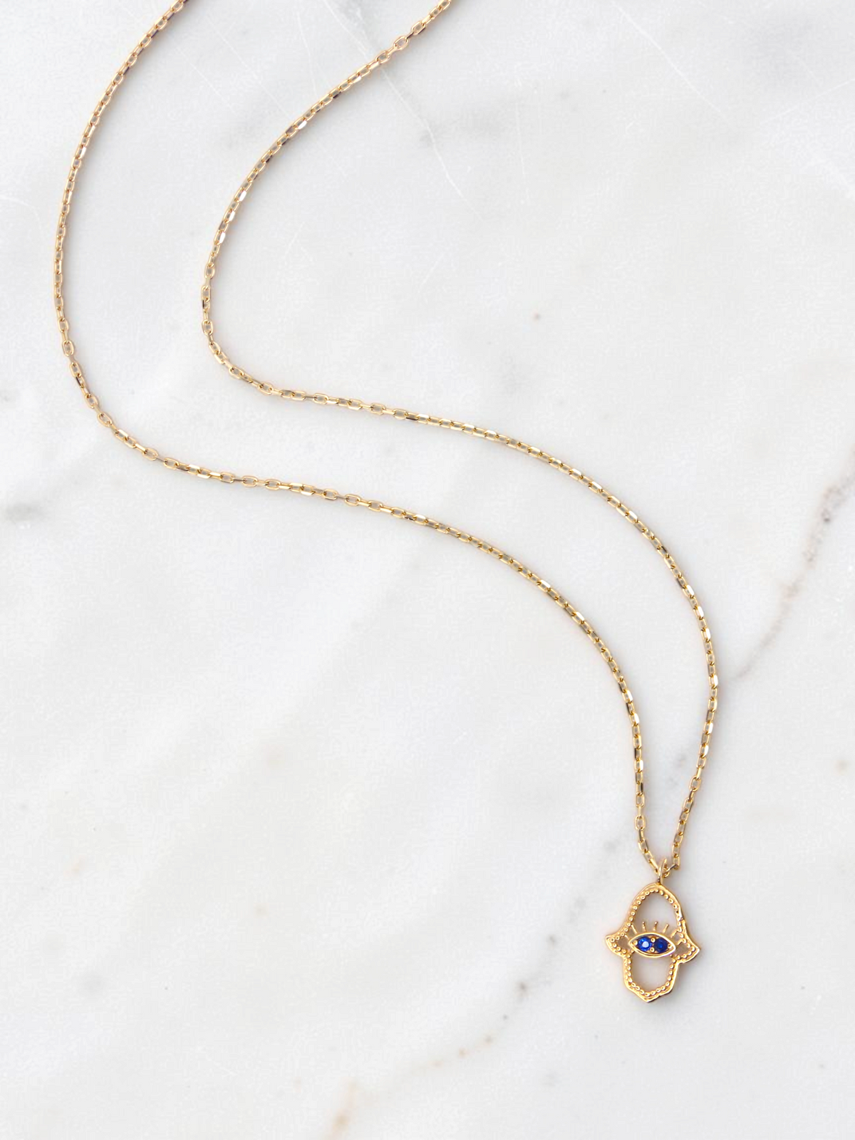 Zafrah 14k yellow gold hamsa eye pendant necklace with two blue stones on a delicate round link chain