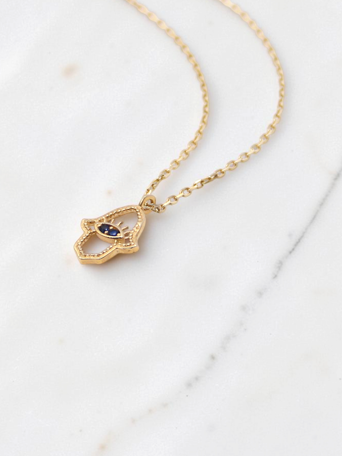 Zafrah 14k yellow gold hamsa eye pendant necklace with two blue stones on a delicate round link chain