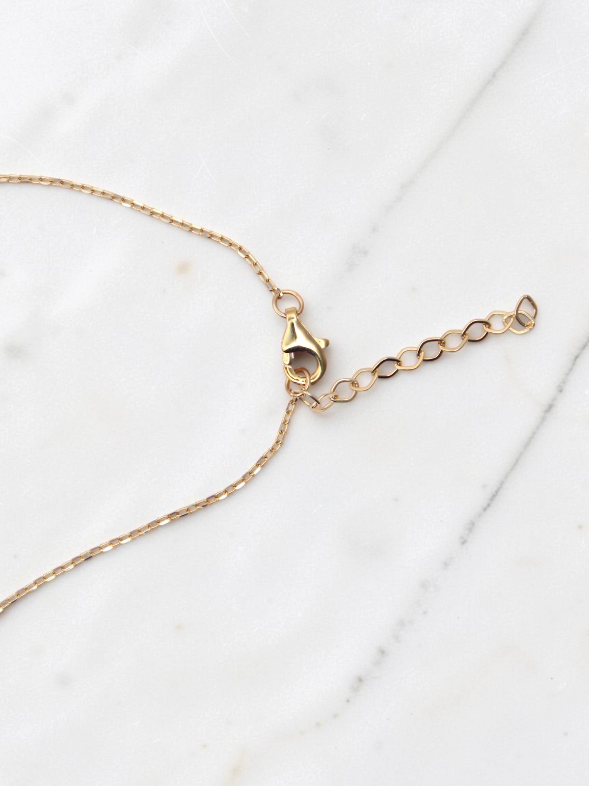 Zafrah 14k yellow gold dainty round link chain with adjustable lobster clasp on a white marble background