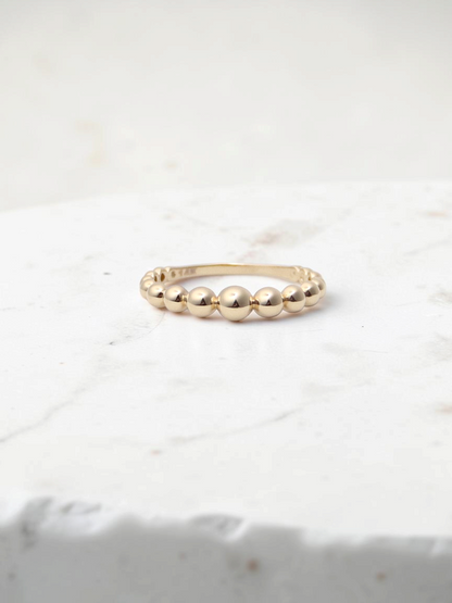 Zafrah 14k yellow gold beaded stacker ring with a polished finish on a white display block
