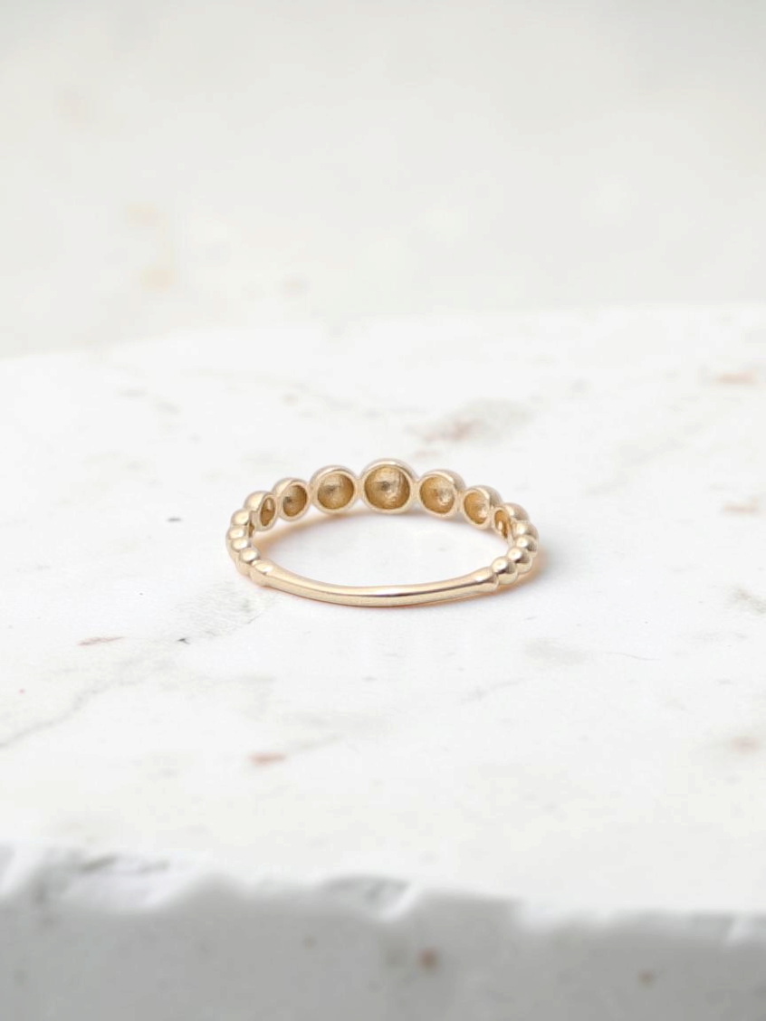 Zafrah 14k yellow gold beaded stacker ring with a delicate textured design on a white surface.