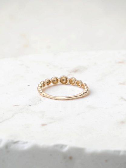 Zafrah 14k yellow gold beaded stacker ring with a delicate textured design on a white surface.