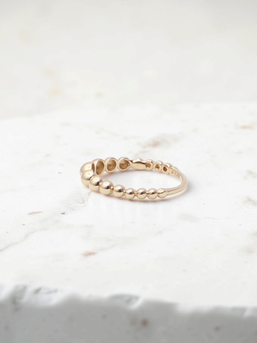 Zafrah 14k yellow gold beaded stacker ring with a delicate textured design on a white surface.