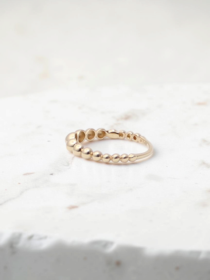 Zafrah 14k yellow gold beaded stacker ring with a delicate textured design on a white surface.