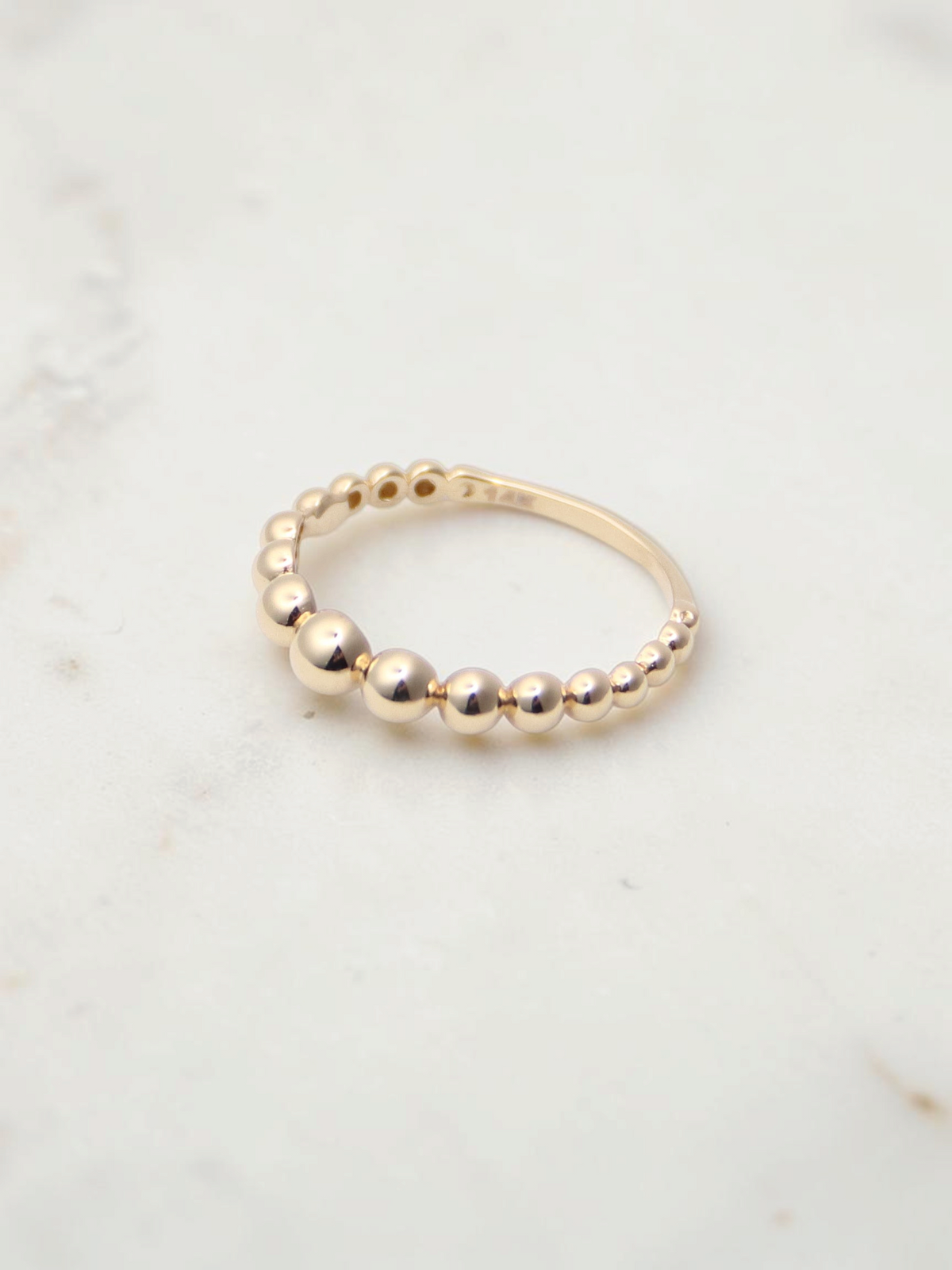 Zafrah 14K yellow gold stacking ring featuring a delicate beaded design on a white marble surface.