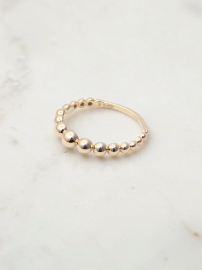 Zafrah 14K yellow gold stacking ring featuring a delicate beaded design on a white marble surface.