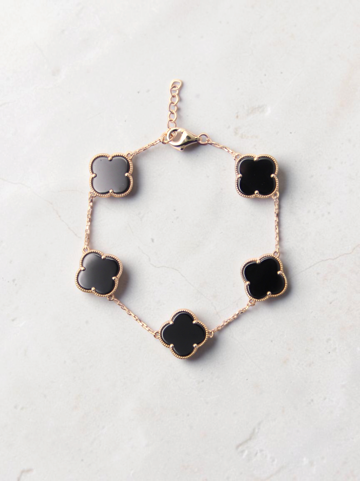 Zafrah gold chain bracelet featuring five black onyx clover motifs on a textured white surface.
