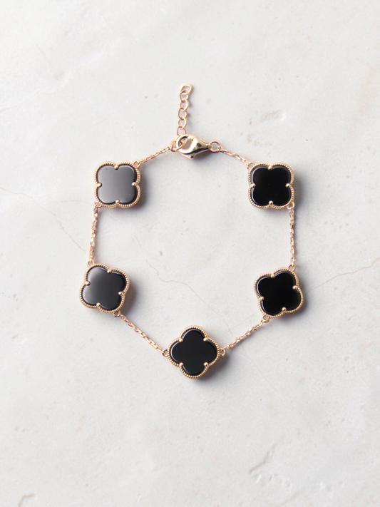Zafrah gold chain bracelet featuring five black onyx clover motifs on a textured white surface.