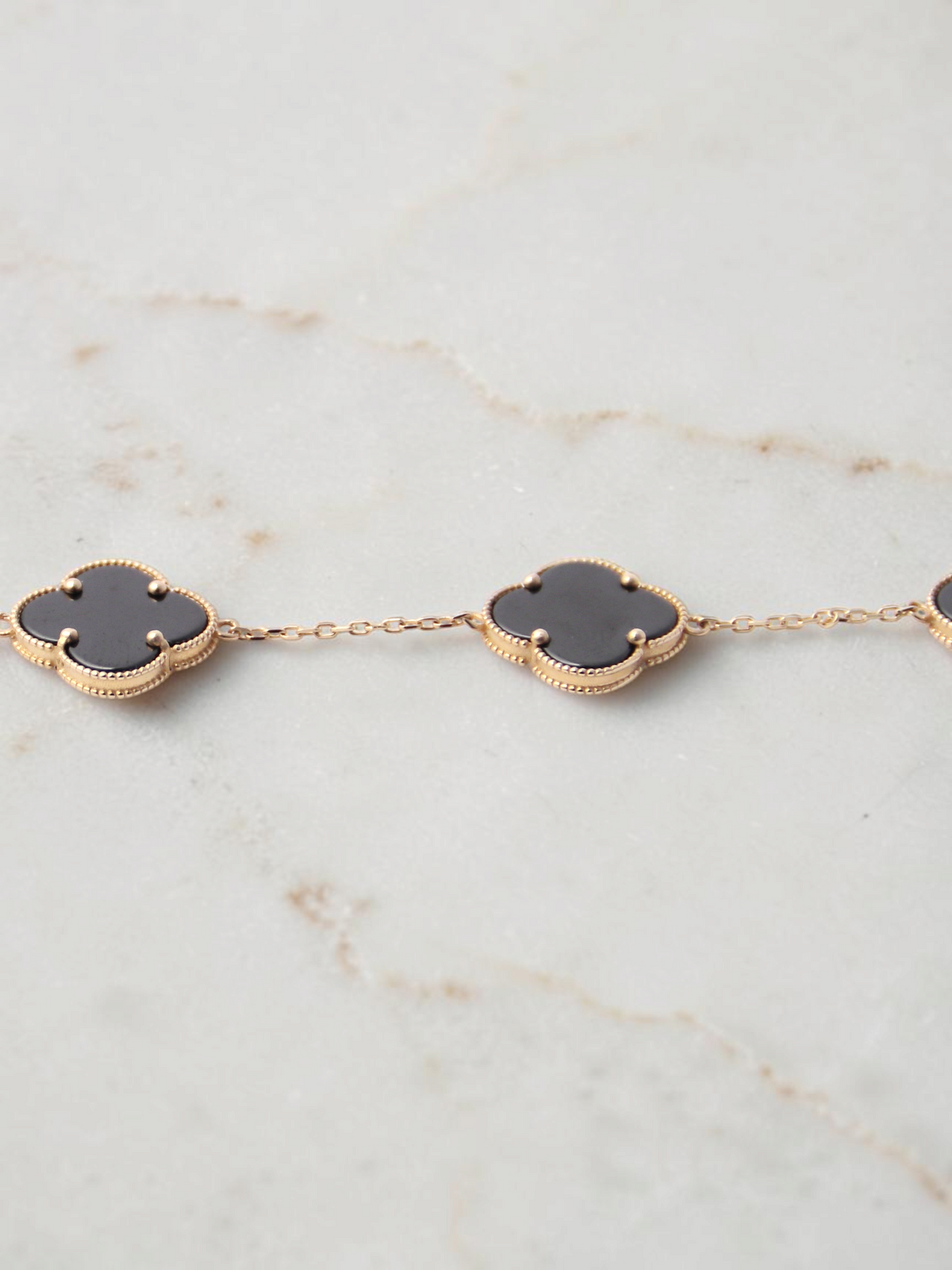 Zafrah gold chain bracelet featuring black onyx clover motifs with delicate beaded edges on a white background