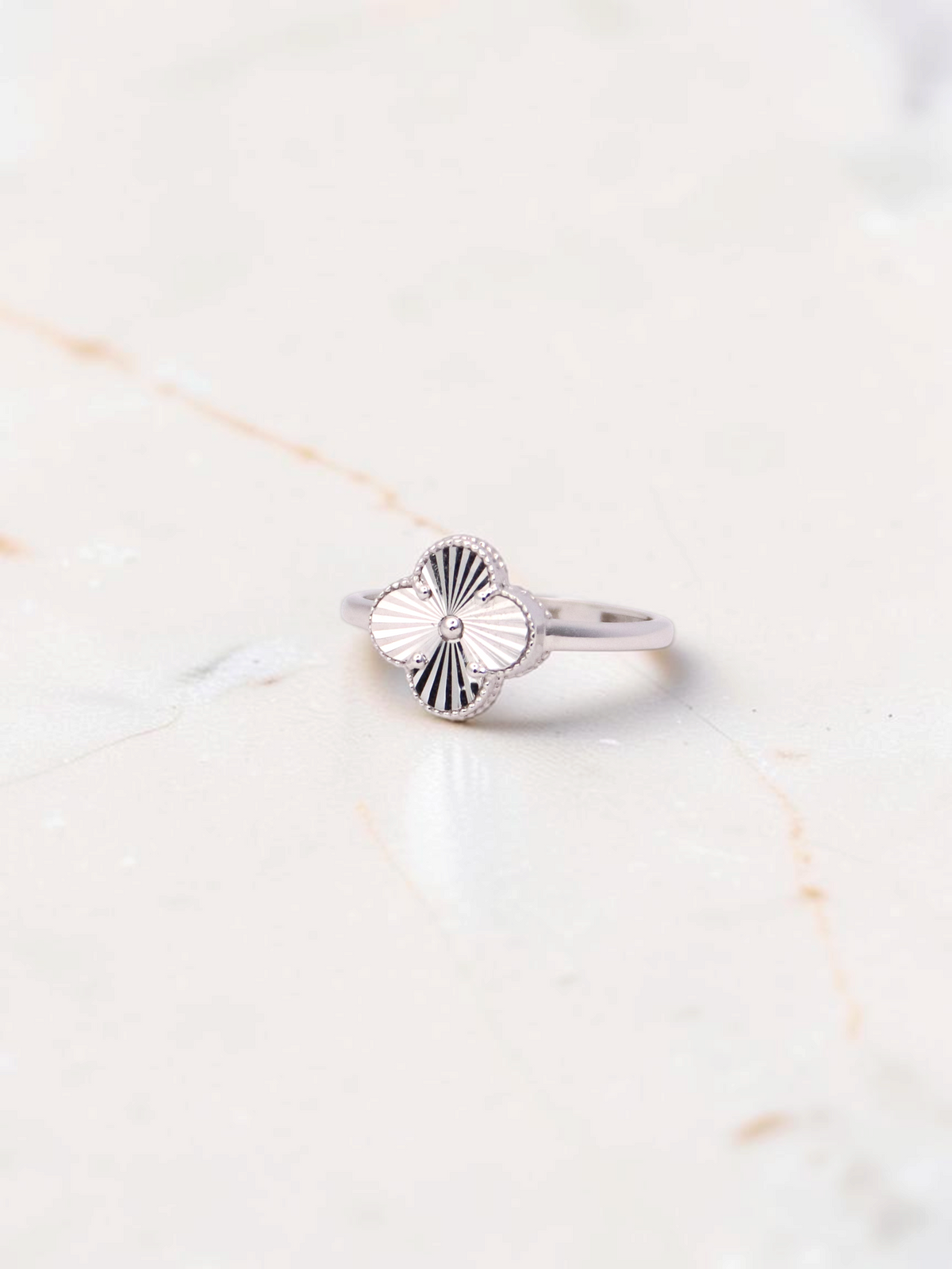 Zafrah 14k white gold Guilloché clover ring with intricate sunburst engraving on a marble surface.