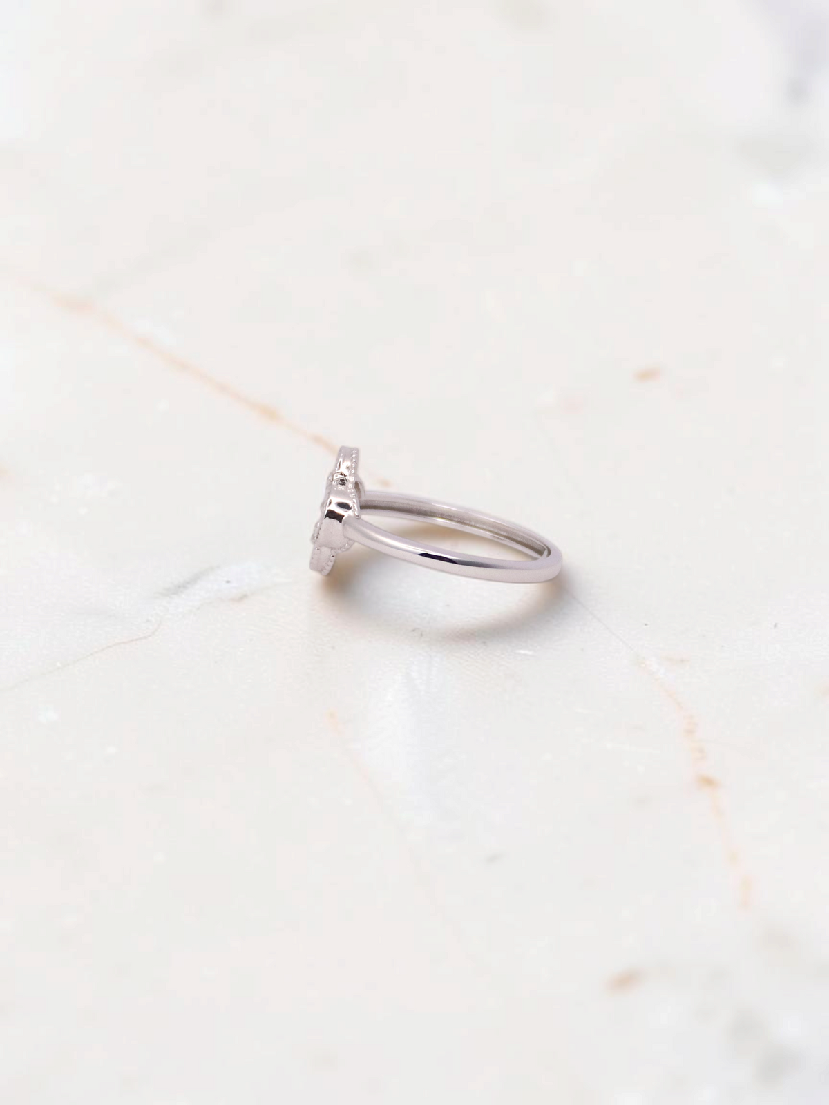 Zafrah 14k white gold Guilloché clover ring viewed from the side on a marble surface.