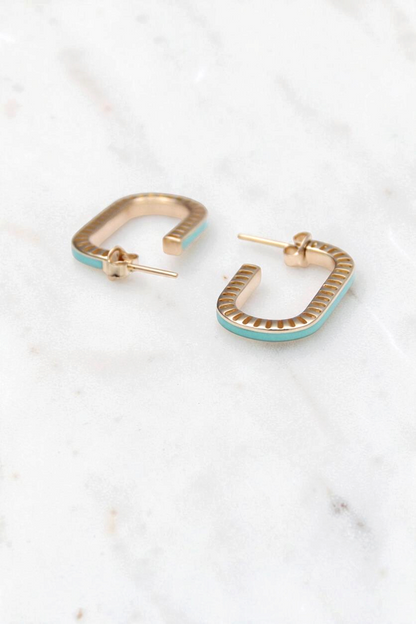 Zafrah 14k gold rectangular stud earrings with curved edges and turquoise enamel inlay on a white marble surface.