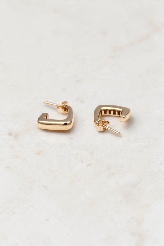 Zafrah 14k solid gold J hoop earrings with a polished finish on a white marble surface