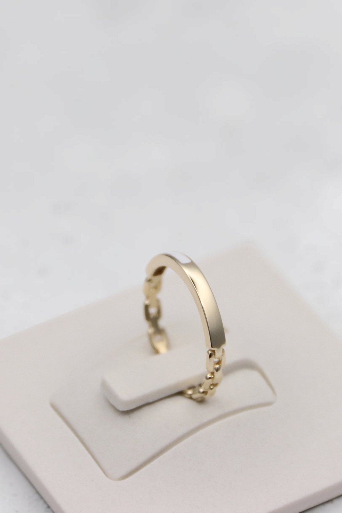 Zafrah 14k solid gold chain link ring with a polished flat band detail on a white display stand