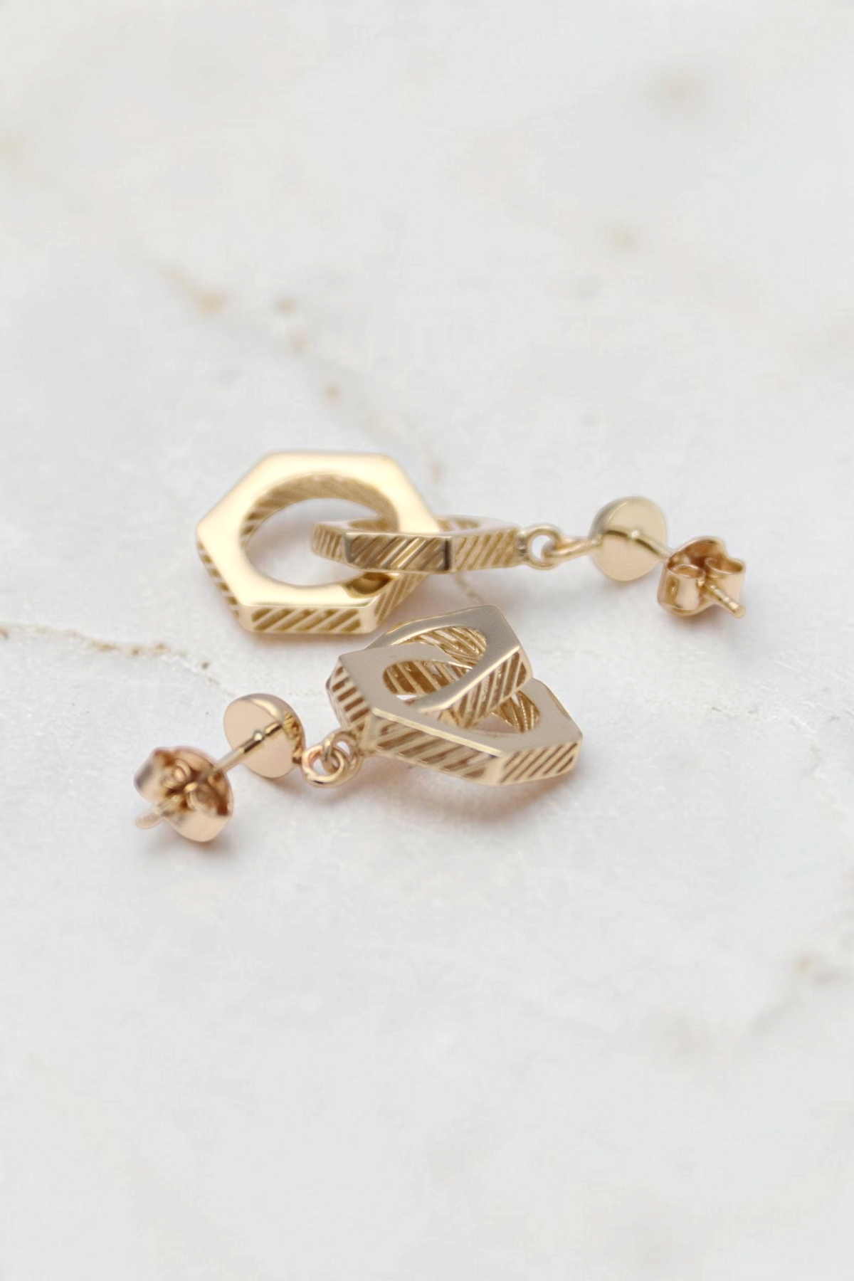 Zafrah 14k solid gold double hexagon drop earrings with industrial textured finish on a white background