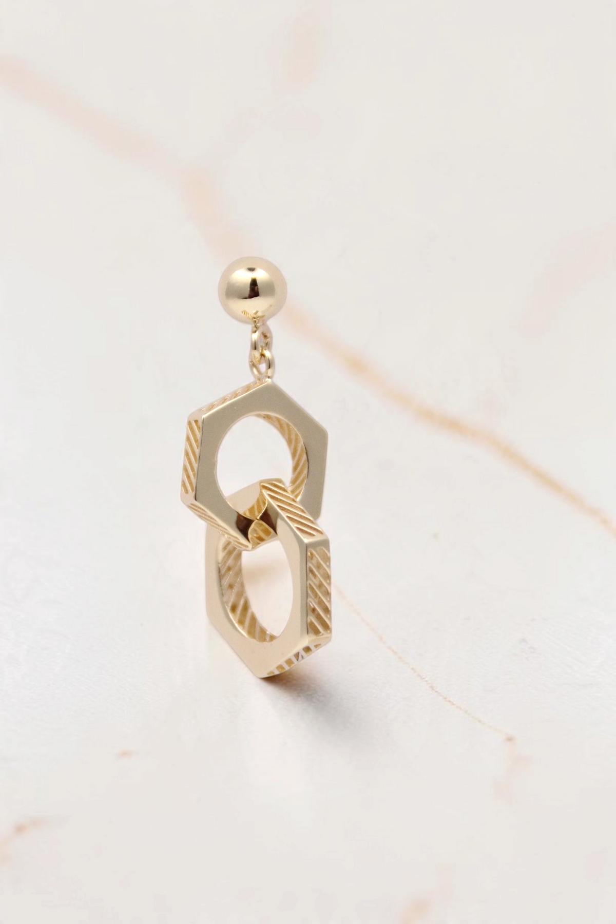 Zafrah 14k solid gold double hexagon drop earrings with industrial textured detailing on a light background