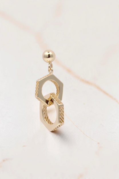 Zafrah 14k solid gold double hexagon drop earrings with industrial textured detailing on a light background