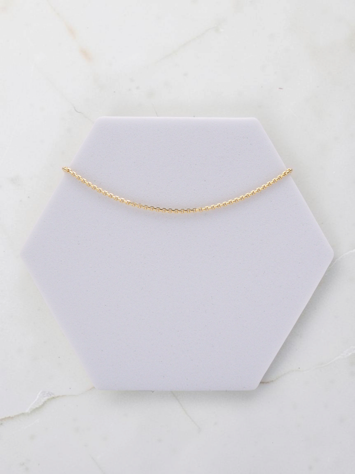 Zafrah 14k yellow gold square rolo chain bracelet, 7 inches long and 1mm wide, displayed on a hexagonal stand.