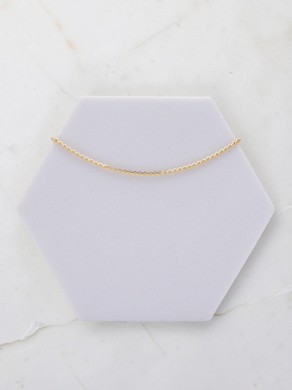 Zafrah 14k yellow gold square rolo chain bracelet, 7 inches long and 1mm wide, displayed on a hexagonal stand.