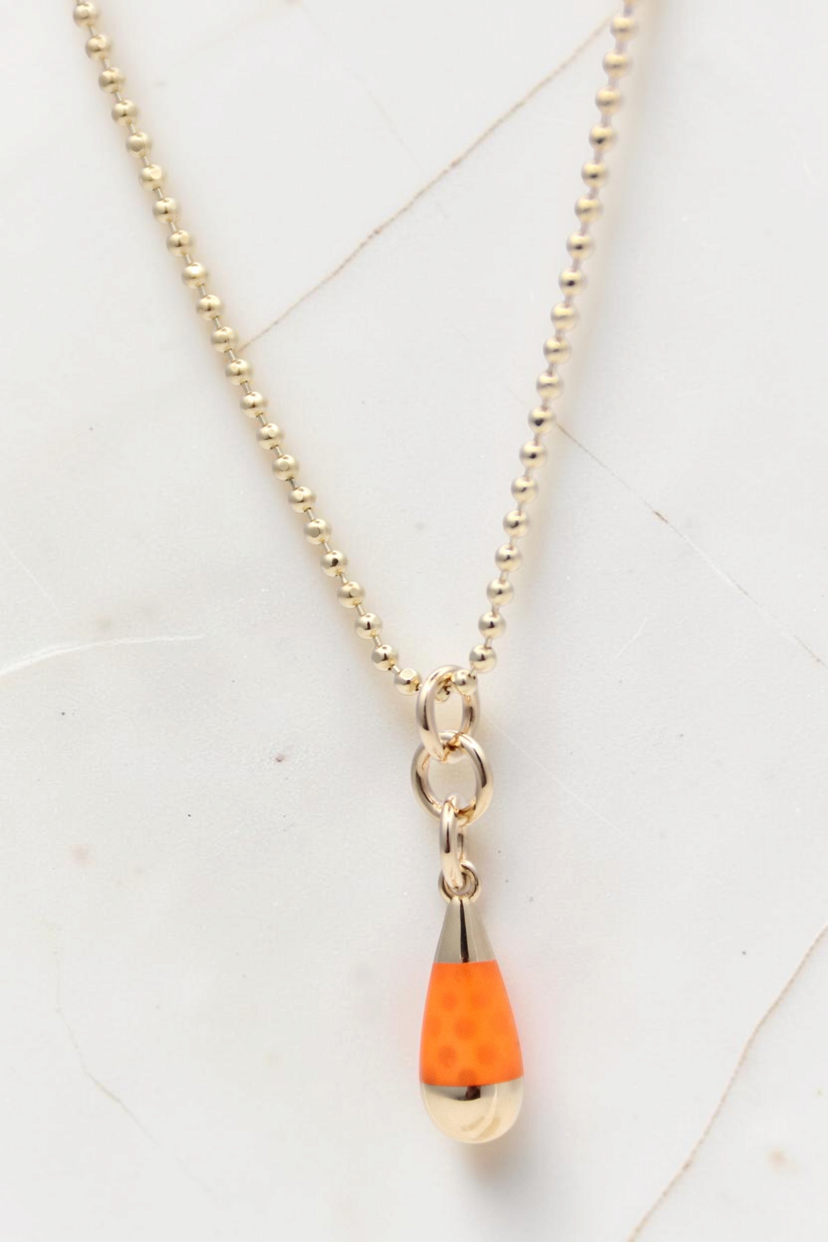 Zafrah 14k gold beaded chain necklace featuring an orange and blue drop pendant on a white marble background.