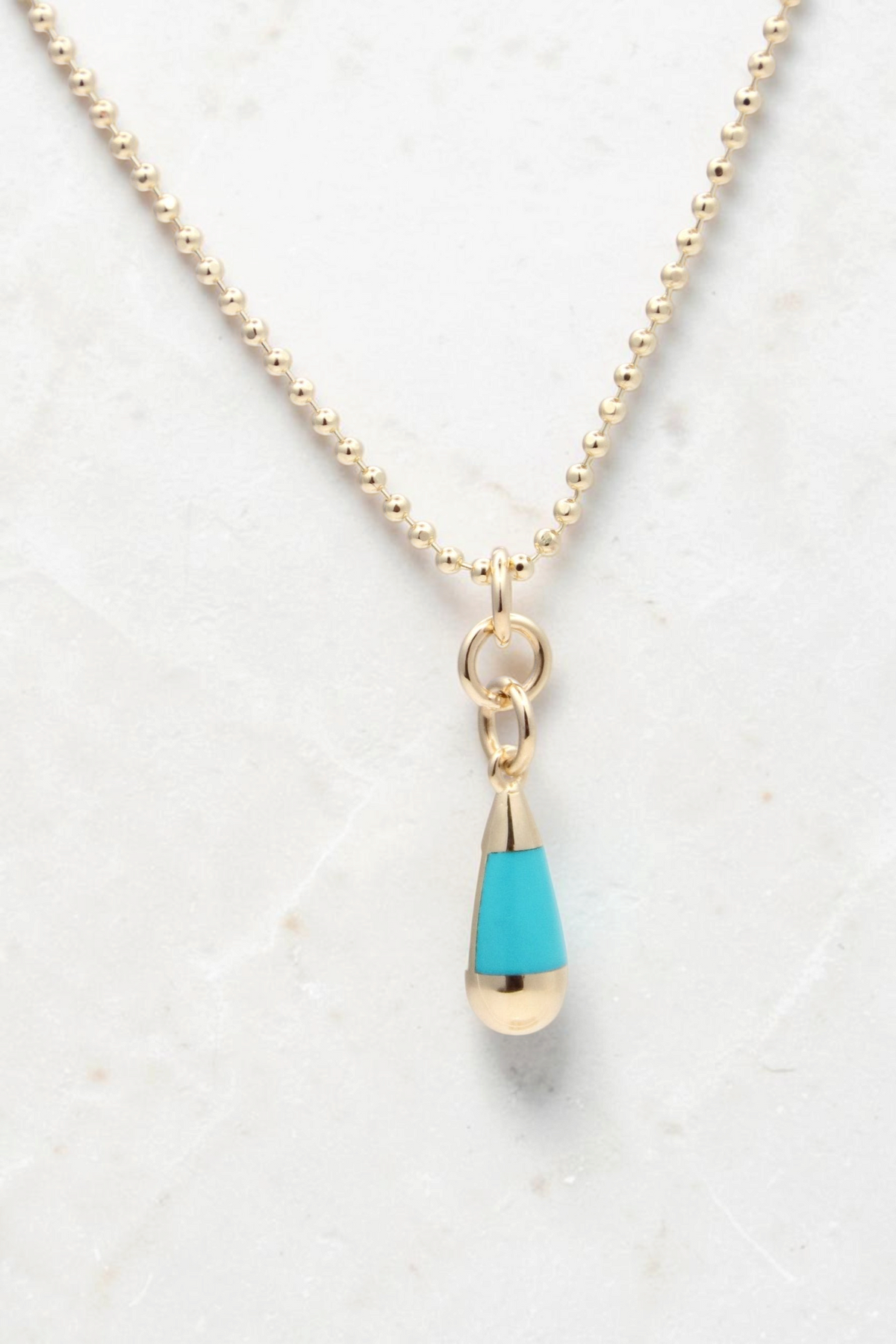 Zafrah 14k gold beaded chain necklace featuring a turquoise and white teardrop pendant on a light background.