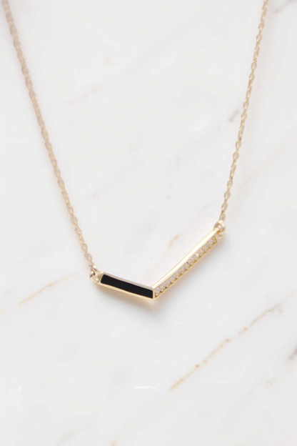 Zafrah 14k gold necklace featuring a V-shaped pendant with one black enamel side and one diamond-accented side.