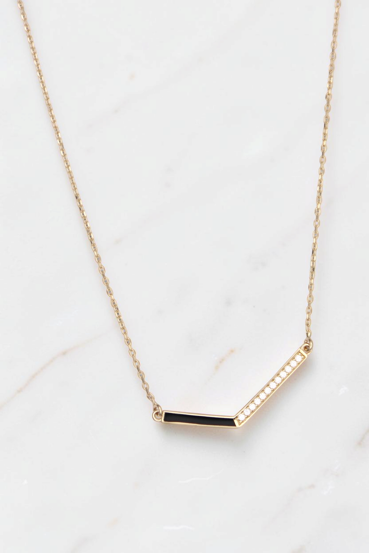 Zafrah 14k gold V-shaped pendant necklace featuring a black enamel inlay and delicate diamond accents on a curb chain.