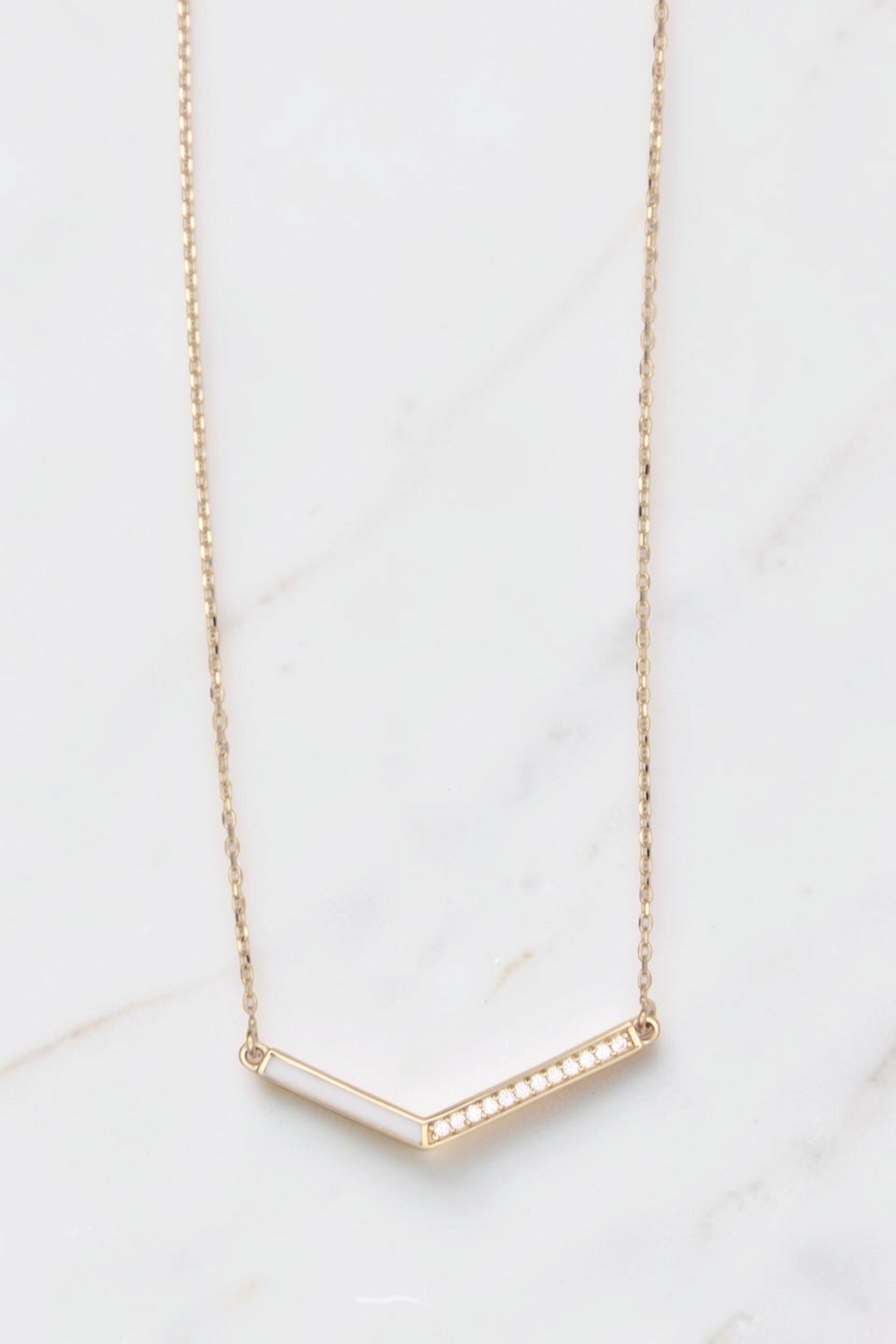 Zafrah 14k gold V-shaped pendant necklace featuring a thin curb chain, white inlay, and delicate diamond accents.