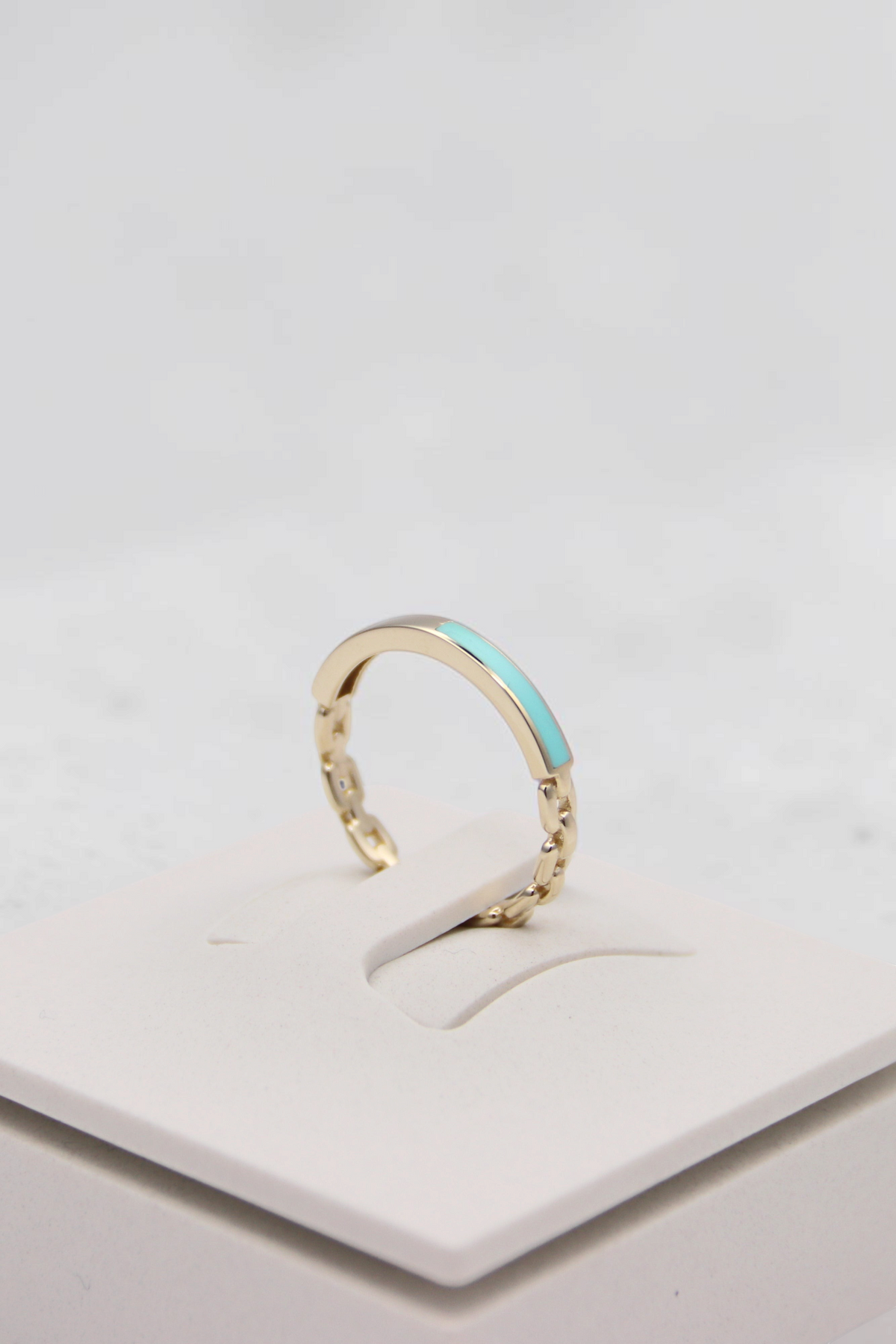 Zafrah 14k solid gold chain link ring with a smooth turquoise enamel inlay on a white display stand