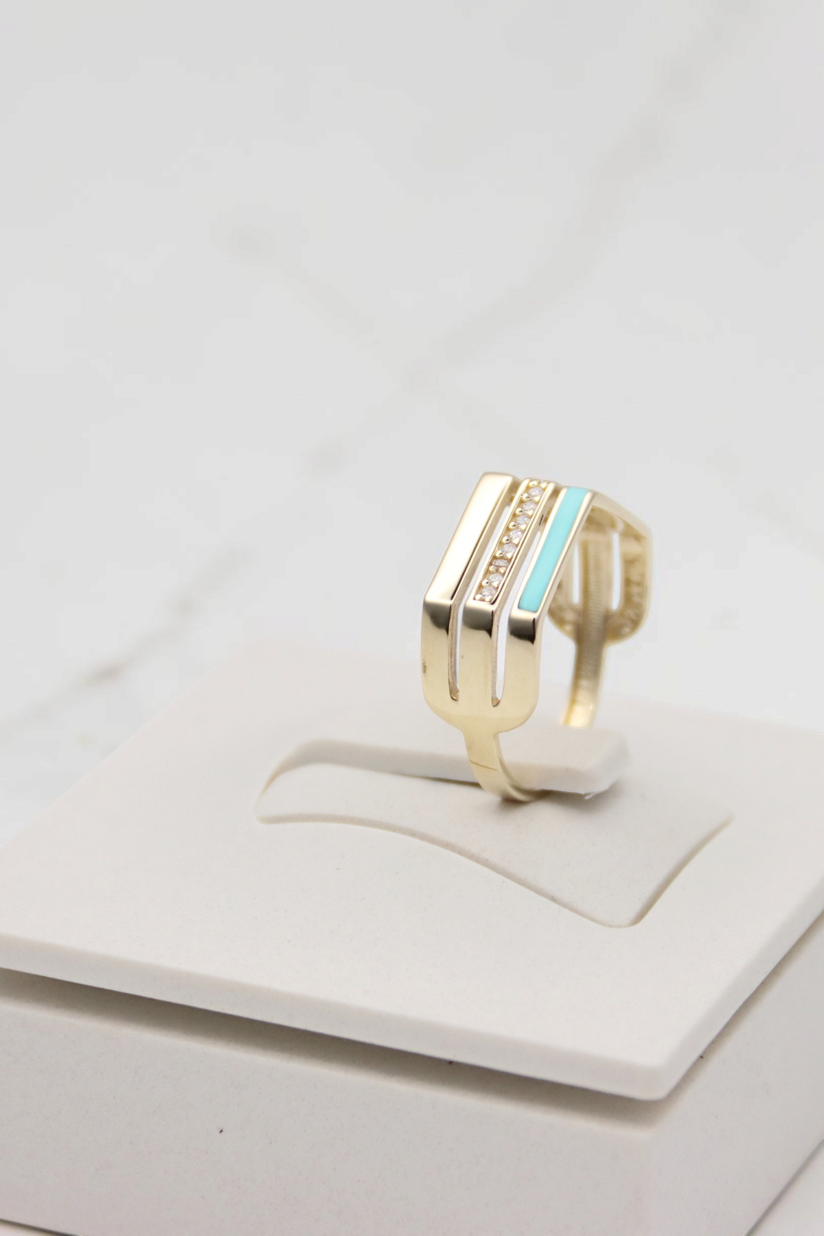 Zafrah 14k solid gold triple line ring featuring a row of diamonds and a turquoise enamel accent on a display stand.