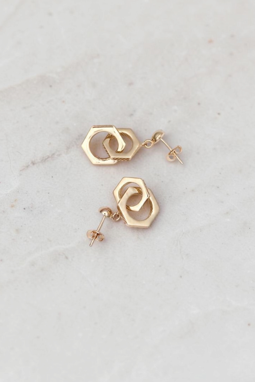 Zafrah 14k solid gold double hexagon drop earrings with a contemporary industrial design on a marble surface