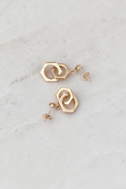 Zafrah 14k solid gold double hexagon drop earrings with a contemporary industrial design on a marble surface