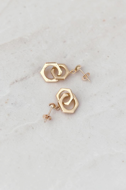 Zafrah 14k solid gold double hexagon drop earrings with a contemporary industrial design on a marble surface