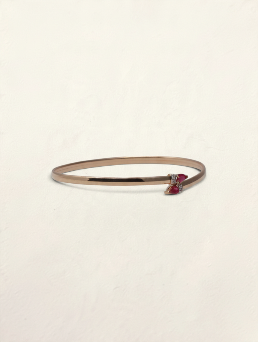 Zafrah 10k yellow gold bypass bangle featuring two pear-cut rubies and small round diamond accents.