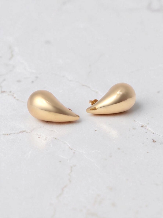 Zafrah chunky teardrop earrings in polished 14k yellow gold on a white marble surface.