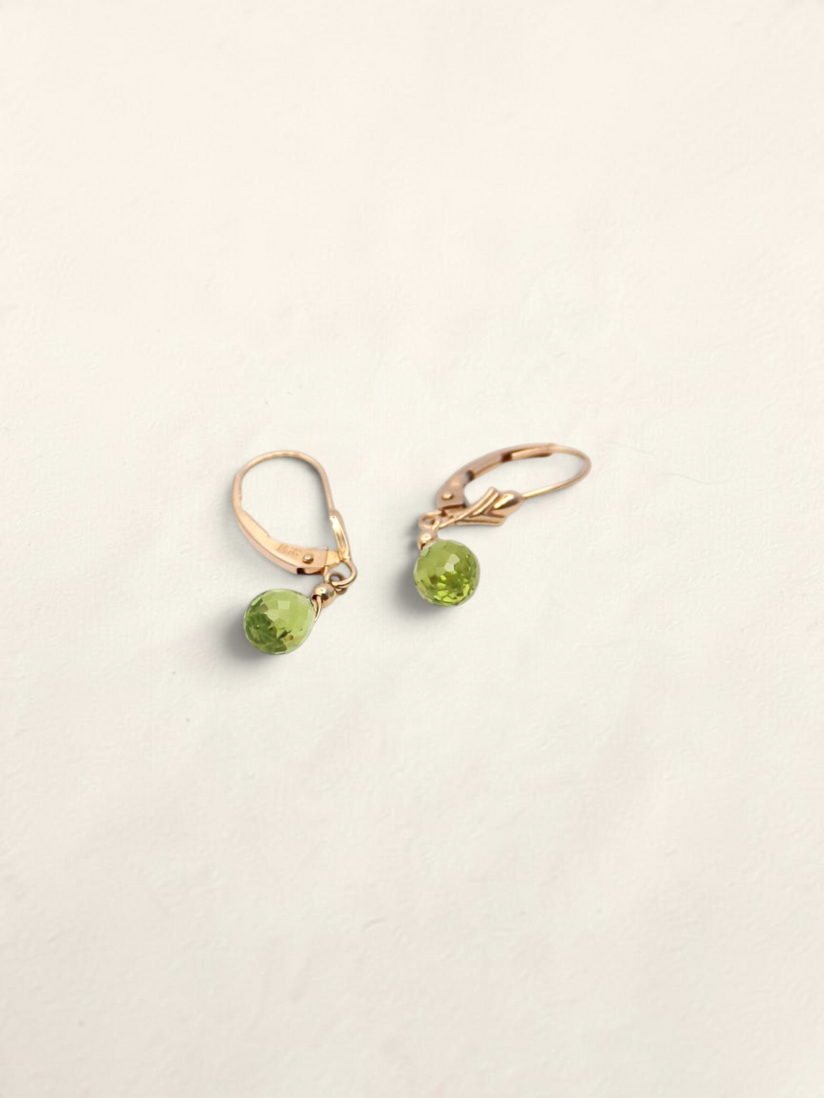 Zafrah 14k yellow gold huggie hoop earrings featuring faceted green quartz drop stones on a neutral background.