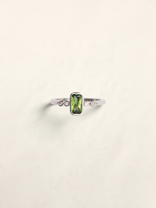 Zafrah platinum ring featuring an emerald cut Australian green sapphire flanked by four round brilliant diamonds.