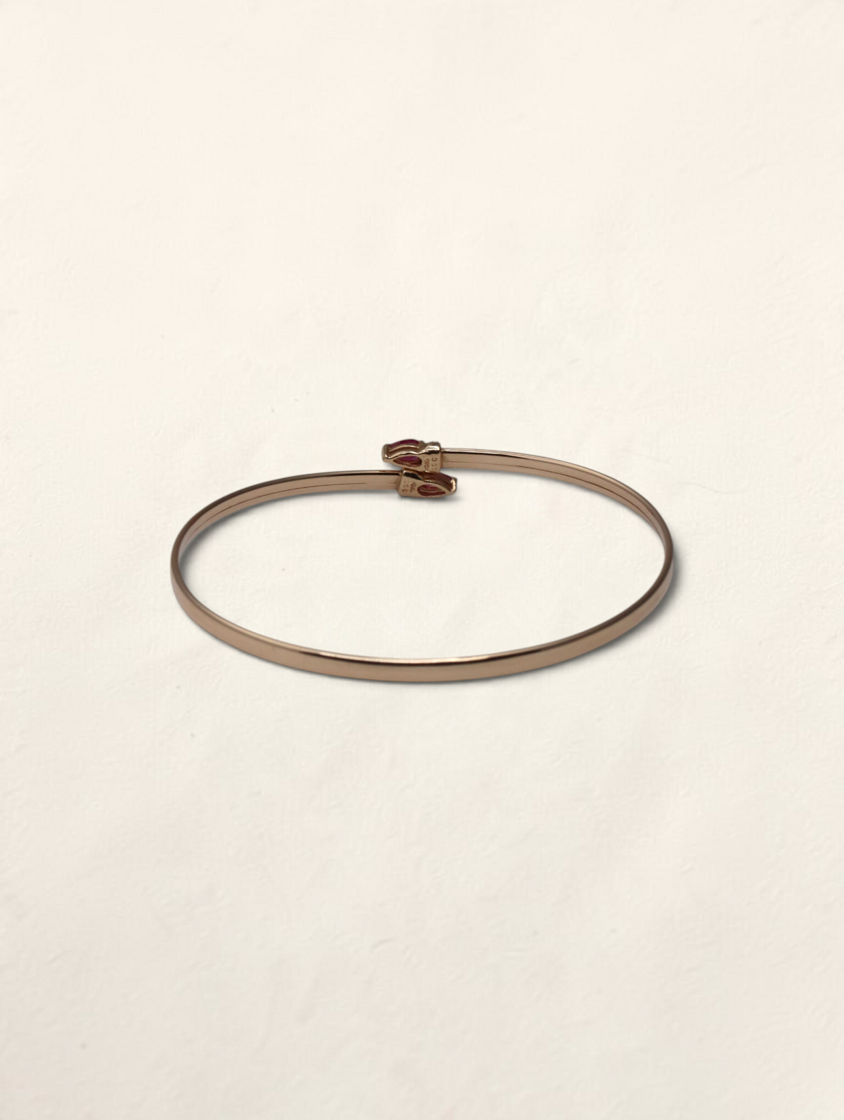 Zafrah 10k yellow gold bypass bangle featuring two pear-cut rubies and small round diamond accents.