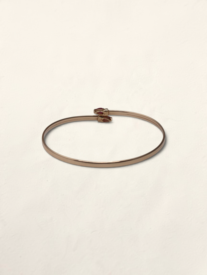 Zafrah 10k yellow gold bypass bangle featuring two pear-cut rubies and small round diamond accents.