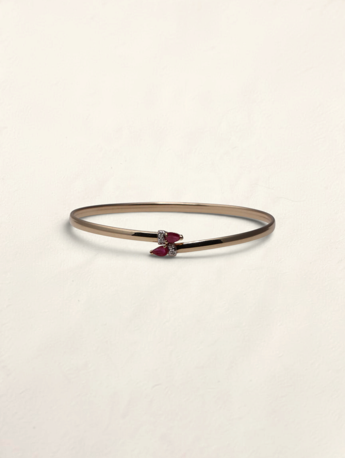 Zafrah 10k yellow gold bypass bangle featuring two pear-cut rubies and small round diamond accents.
