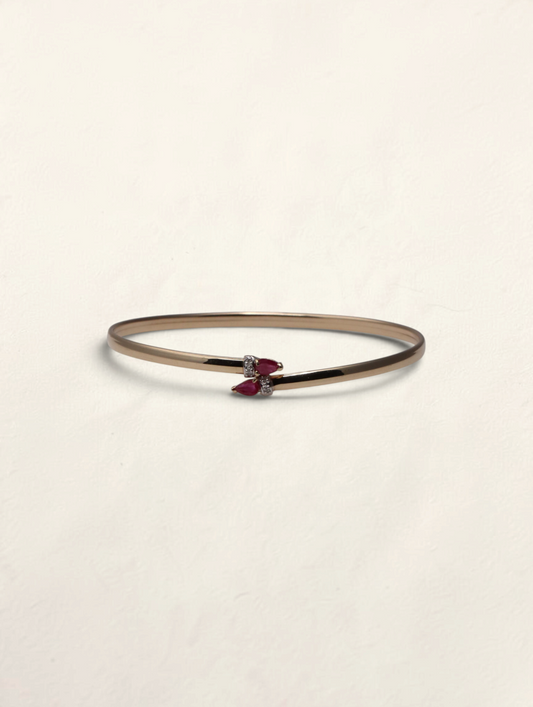 Zafrah 10k yellow gold bypass bangle featuring two pear-cut rubies and small round diamond accents.